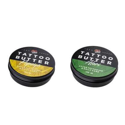 Two tins of Love Ink Tattoo Butter on a transparent background. One tin is labeled 'Aloe' with a green design, and the other is labeled 'Papaya' with an yellow design. Both tins are 100 ml and are intended for after tattooing and daily care.