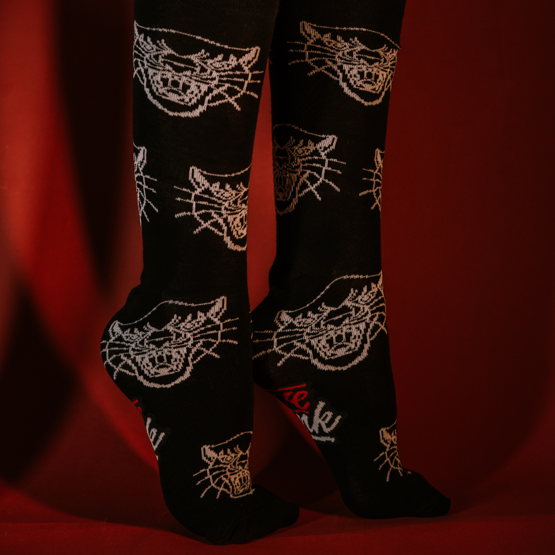 Feet wearing black LOVEINK socks with a white panther head design, posed against a red background.