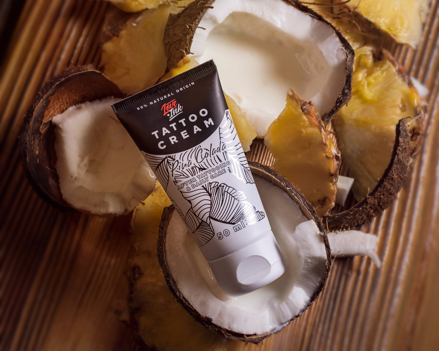 Tube of Tattoo Cream by LoveInk placed among coconut and pineapple pieces, highlighting the tropical ingredients.