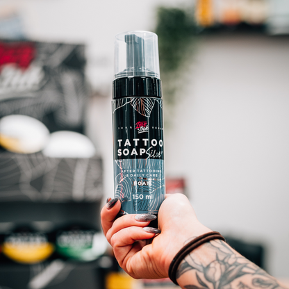 Close-up of a hand holding LoveInk's Tattoo Soap Silver bottle. The product is for daily tattoo care and has a capacity of 150ml.